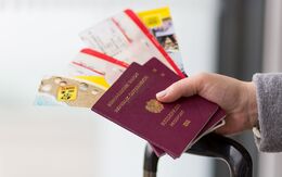 Eine Hand hält zwei österreichische Reisepässe, Tickets und Folder, darunter sieht man den Griff von einem Koffer.