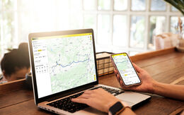 Eine Person nutzt einen Laptop und ein Smartphone mit der ÖAMTC-App zur Routenplanung.