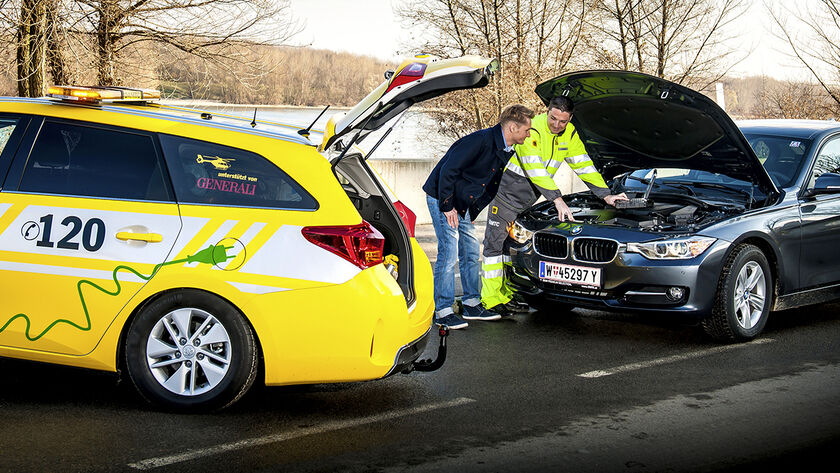 ÖAMTC Techniker mit Mitglied vor geöffneter Motorhaube auf winterlicher Straße