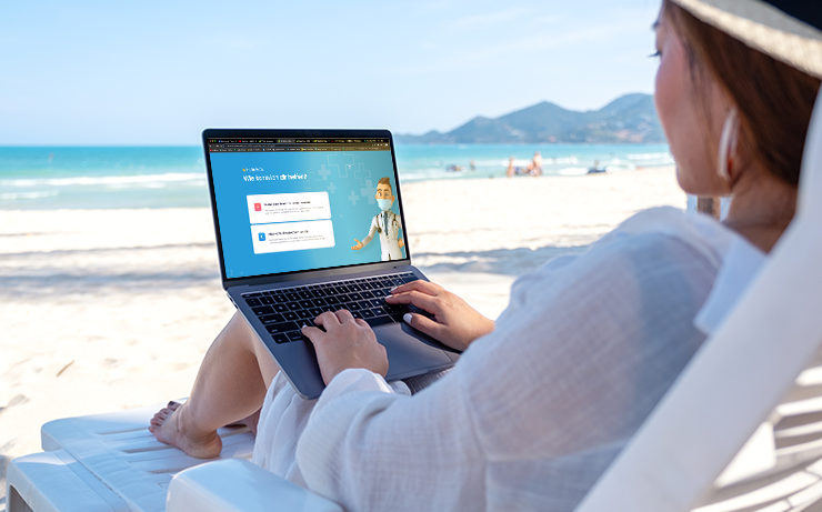 Person arbeitet mit Laptop auf einer Strandliege, im Hintergrund Strand und Meer.