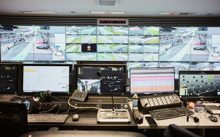 Der Race-Controll-Room des Red Bull Rings mit einer Wand voller Bildschirme, im Vordergrund befinden sich viele Laptops und Tastaturen.