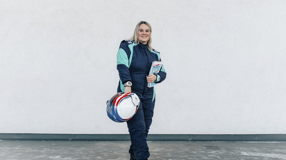 Catharina Schmidt, Rallye-Co-Pilotin und ÖAMTC-Mitarbeitetin steht im Renndress und mit Haube vor hellgrauem Hintergrund und Helm in der Hand.