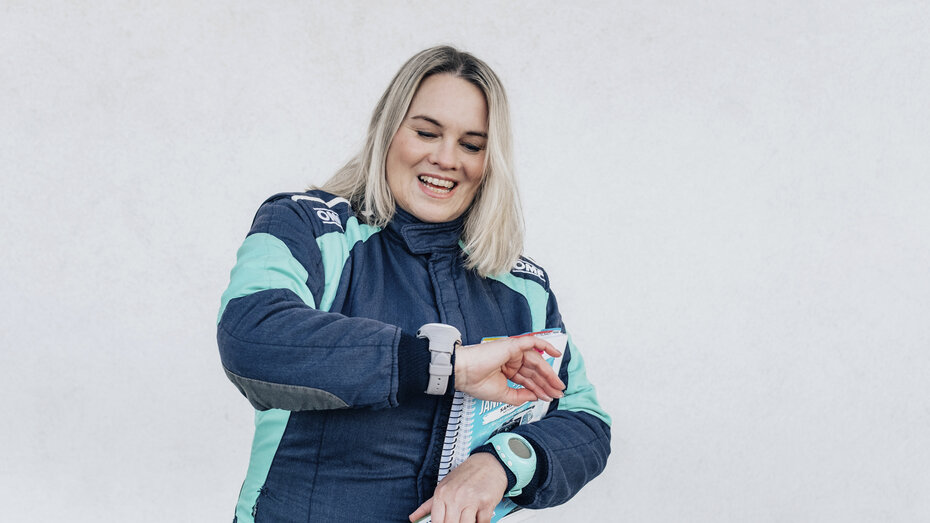 Catharina Schmidt, Rallye-Co-Pilotin und ÖAMTC-Mitarbeitetin steht im Renndress vor hellgrauem Hintergrund.