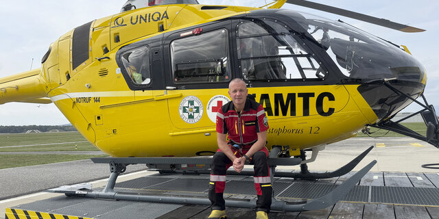 Flugretter Markus Amon sitzt in seiner Uniform vor einem Christophorus Helikopter.