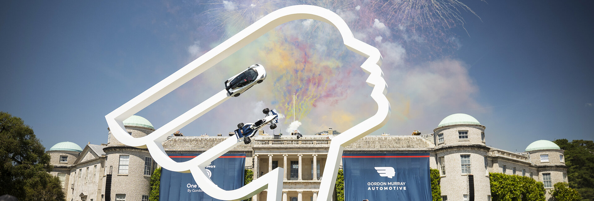 Feuerwerk über einem Schloss. Davor steht ein Kunstwerk mit zwei Fahrzeugen.