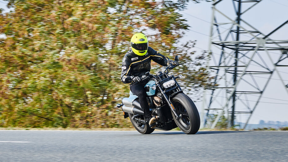 Schräg von vorne fotografiertes Motorrad, das mit leichter Schräglage durch eine Kurve fährt.