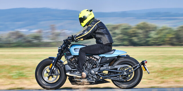 Seitlich fotografiertes, fahrendes, blau-schwarzes Motorrad.