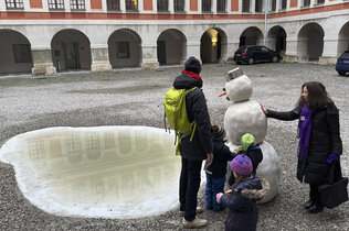 Der Schneemann aus Stein samt Regenlacke wird von den Kindern, dem Papa und der Fremdenführerin betaunt.