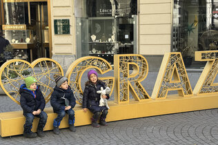 Die Drillinge sitzen in der Stadt auf dem Schriftzug "I love Graz"