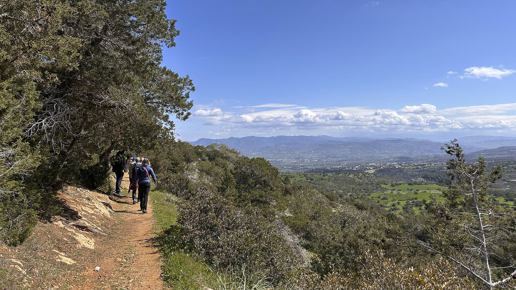 Wandernde gehen im Akamas-Naturpark auf rotem Erdpfad entlang, Im Hintergrund das Meer.