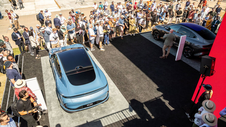 Eine blaue Limousine steht auf einer Bühne, drumherum befindet sich eine Menschenmasse.