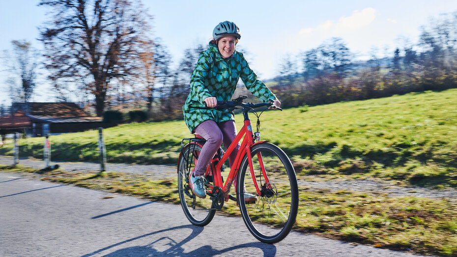 Hebamme Martina Klasz fährt mit dem E-Bike am Radweg neben einer Wiese.