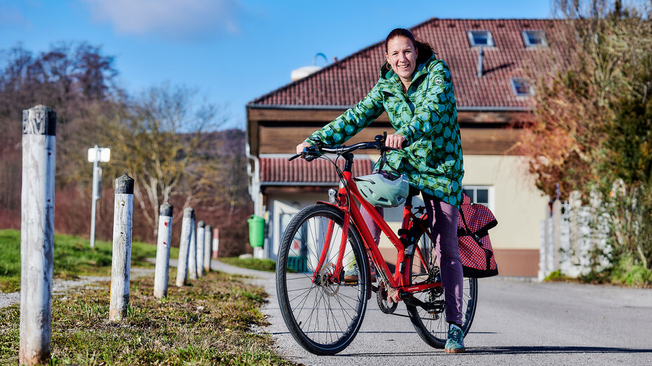 Eine Frau, die  sitzt auf einem Fahrrad, im Hintergrund ein Wohnhaus.