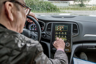 Innenansicht eines Autos. Ein Mann bedient die Klimaanlage am Display.