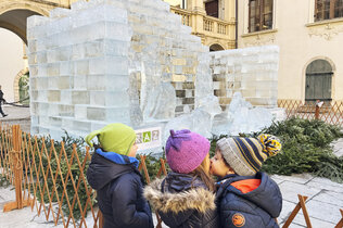 drei Kinder stehen vor der Eiskrippe und zwei Kids geben sich ein Bussi.