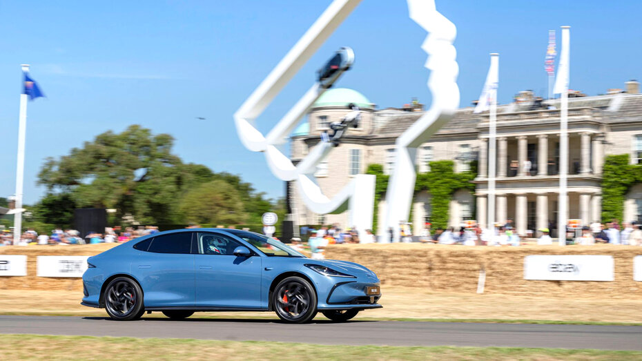 Eine blaue Limousine fährt über die Goodwood-Hillclimb-Strecke am Goodwood Haus vorbei.