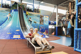 Große Rutsche beim Klettervulkan auf der ein Mann gerade herunterrutscht am Indoor-Spielpatz