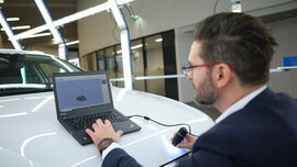 Michael Planer kontrolliert mit einem Laptop die Motorhaube eines Autos