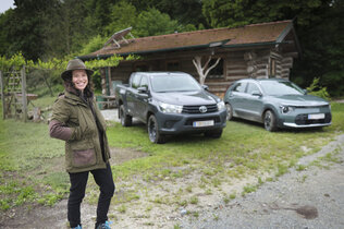 Försterin Stefanie Nievoll steht vor ihren Dienstfahrzeugen Kia Niro. Im Hintergrund der zweite Dienstwagen, ein Toyota Hilux und eine Blockhütte.