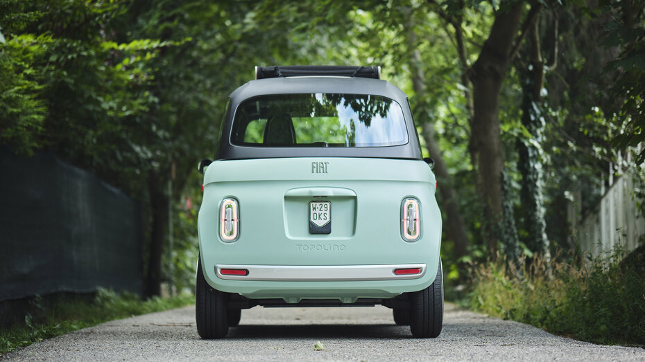 Ein türkises Microcar steht auf einer Straße, die von Bäumen umgeben ist.