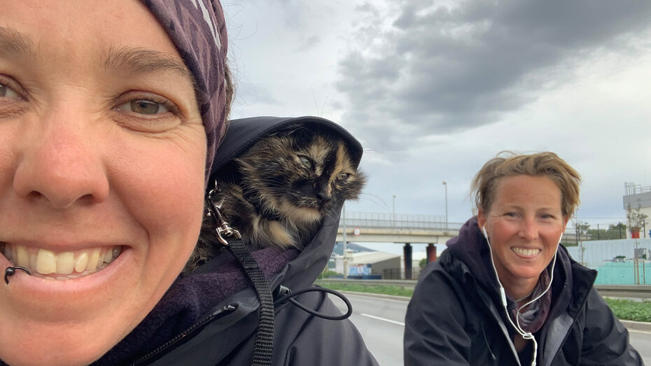 Selfie von Tanja Willers. Im Vordergrund ist sie zu sehen, auf ihrer Schulter sitzt eine Katze, daneben ihre Partnerin Johanna. Im Hintergrund eine Brücke.