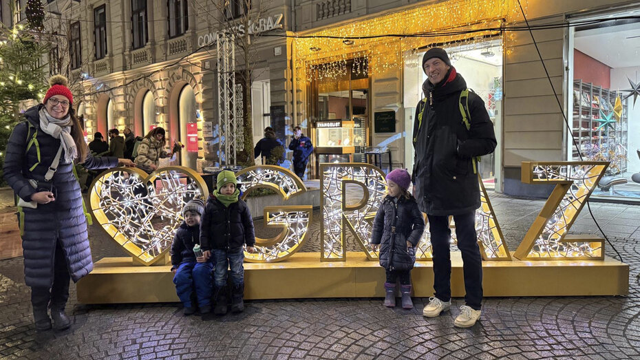 Familie mit drei Kids steht in der Nacht vorm beleuchteten Graz-Schriftzug.