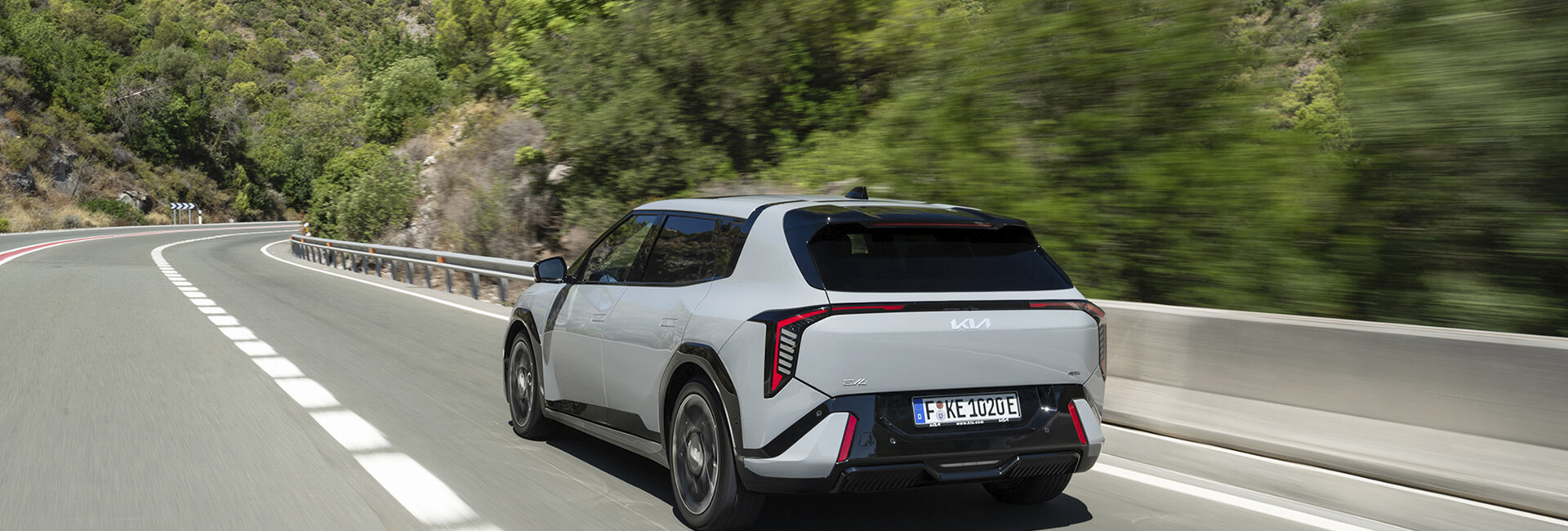 Ein grauer Kia EV4 fährt über eine Landstraße.