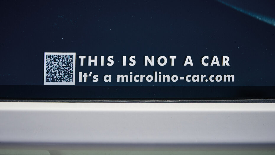 Ein Aufkleber mit QR-Code, der "This is not a car. It's a microlino-car.com"  besagt, auf dem Seitenfenster des Kleinfahrzeuges Microlino,