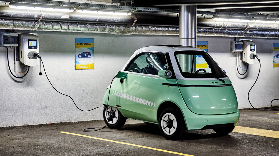 Das Kleinfahrzeug Microlino in hellgrün steht an einer Ladestation angesteckt in einer Garage.