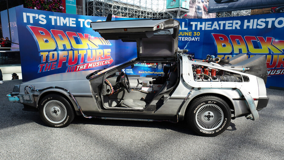 Ein silberner Sportwagen mit Umbauten steht vor einem "Back to the Future"-Plakat
