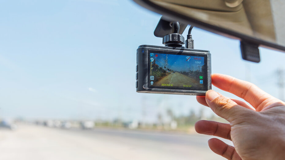 Eine Hand greift zu einer Dashcam an der Windschutzscheibe eines Autos