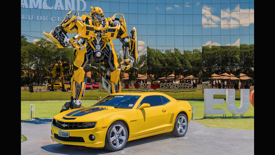 Ein gelbes Auto steht vor einer überlebensgroßen Transformers-Figur