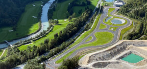 Inmitten einer ländlichen Landschaft erstreckt sich das Experience Center Saalfelden/Brandlhof. Eine große asphaltierte Übungsfläche, mit Kreuzungselementen und Übungsstraßen. Links der Übungsfläche sind eine Bundesstraße, Wiesen, ein Fluss mit zwei Brücken und ein anschließender Wald.