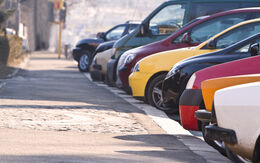 Eine Reihe verschiedener Autos, die vor einem Gehsteig eng nebeneinander geparkt sind.