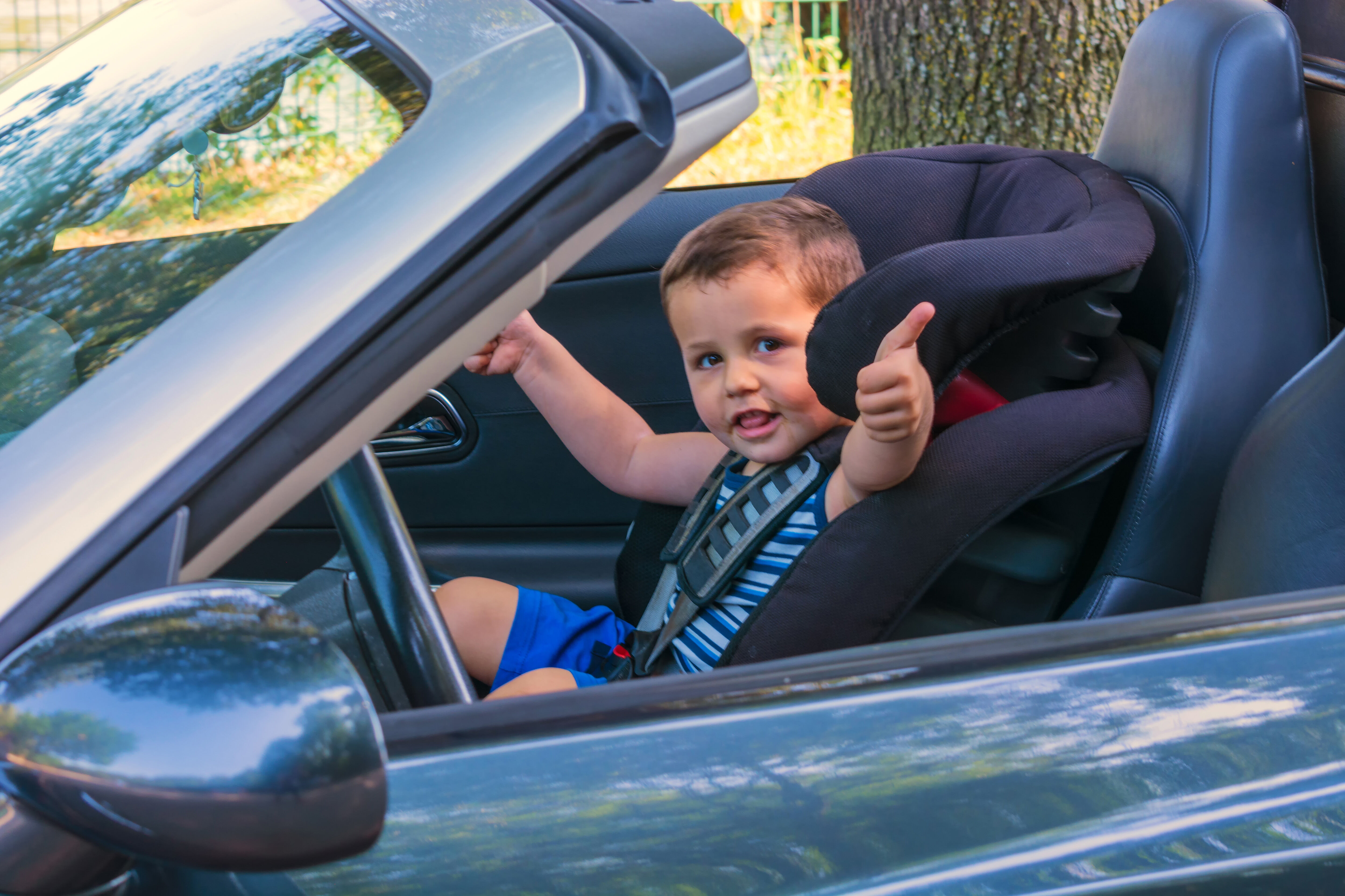 Ein kleines Kind sitzt gesichert in einem nach vorne gerichteten Kindersitz auf dem Beifahrersitz eines Autos. Das Kind lächelt und scheint zufrieden zu sein