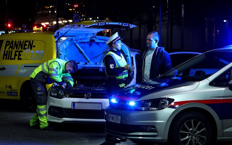 Polizistin klärt Autofahrenden über die Wichtigkeit einer ausreichenden Beleuchtung auf. Im Hintergrund wird von einem ÖAMTC-Techniker die Lampe beim Auto getauscht. Die gemeinsame Aktion nennt sich Licht statt Strafe.