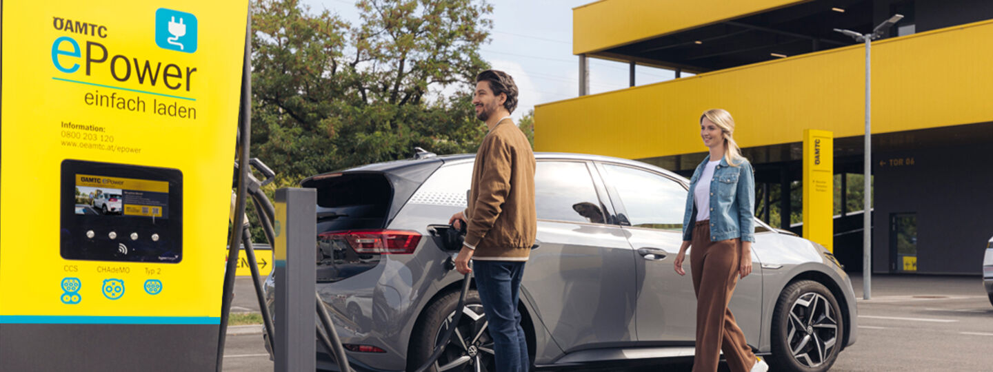 Zwei Personen, die ein Elektroauto an einer ÖAMTC ePower-Ladesäule anschließen, um den Akku aufzuladen.