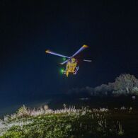 Ein gelber Notarzthubschrauber schwebt nachts über einer grünen Wiese.