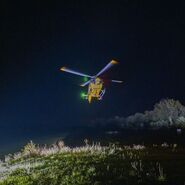 Ein gelber Notarzthubschrauber schwebt nachts über einer grünen Wiese.