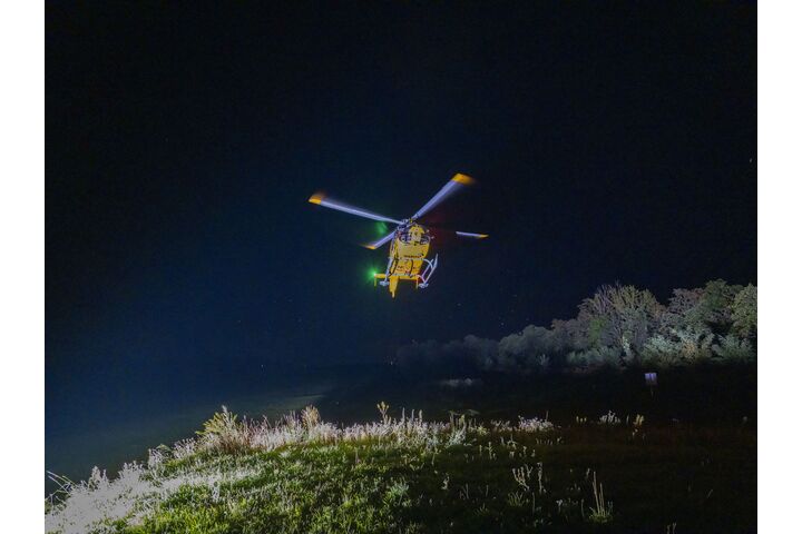 Ein gelber Notarzthubschrauber schwebt nachts über einer grünen Wiese.
