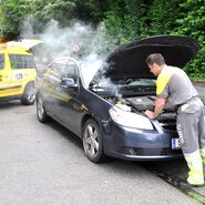 Pannenfahrer vor geöffneter Motorhaube, eine weitere Person steht daneben