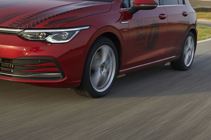 Auf dem Bild ist ein Teil eines roten Autos zu sehen, das durch eine Landschaft fährt. Auf der Tür des Autos steht in schwarzer Schrift "50 Jahre Reifen-Test".