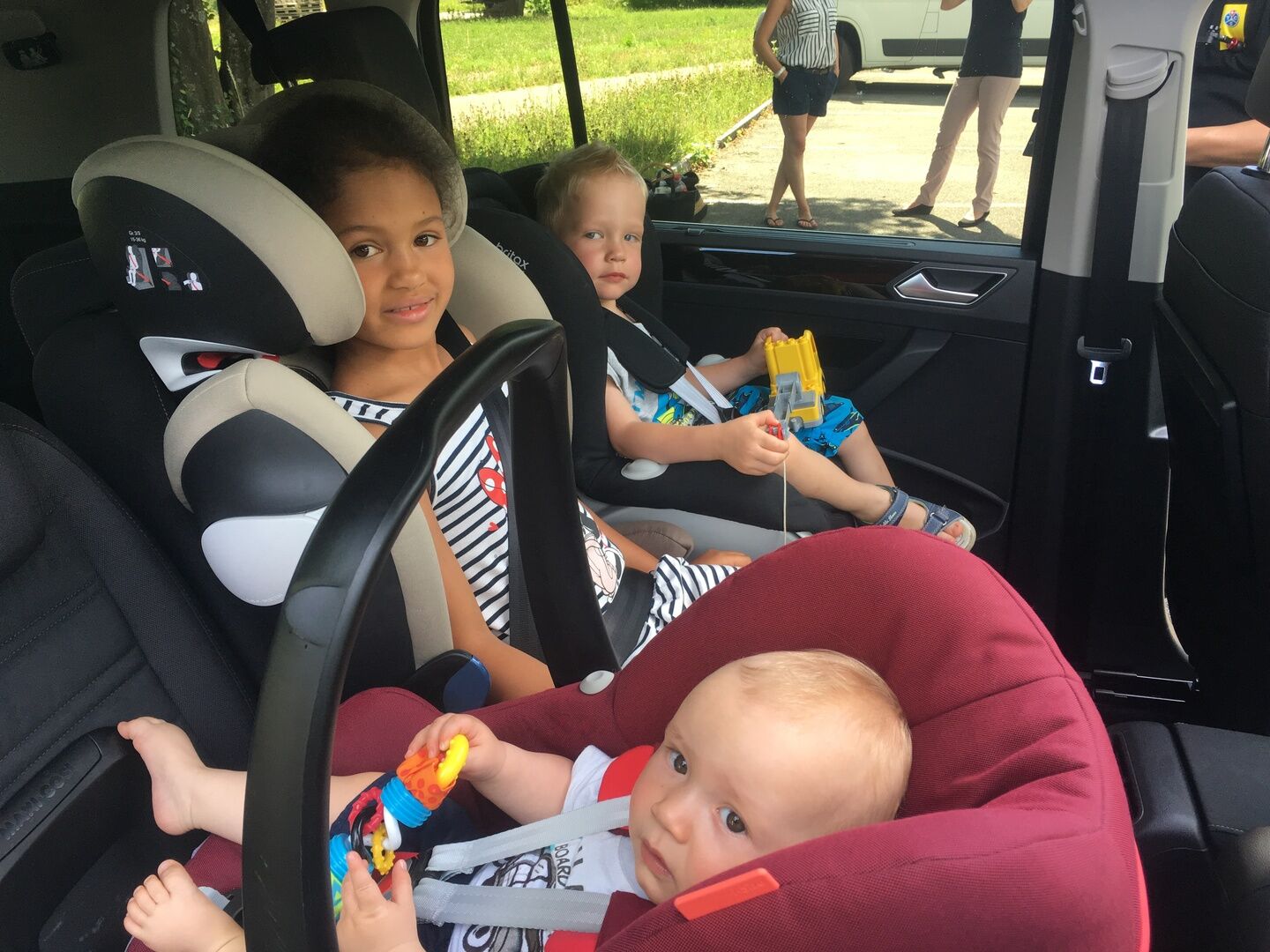 Drei Kinder sitzen sicher in ihren Kindersitzen auf der Rückbank eines Autos.