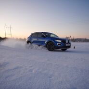 Ein Testfahrzeug driftet mit Winterreifen auf winterlicher Fahrbahn während die Sonne untergeht 