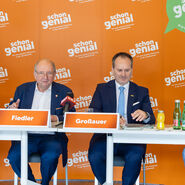 Vier Herren im Anzug sitzen an einem Tisch und geben eine Pressekonferenz