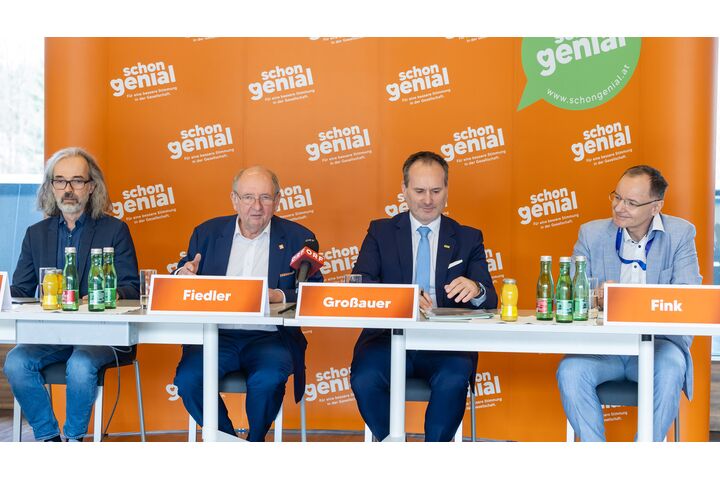 Vier Herren im Anzug sitzen an einem Tisch und geben eine Pressekonferenz