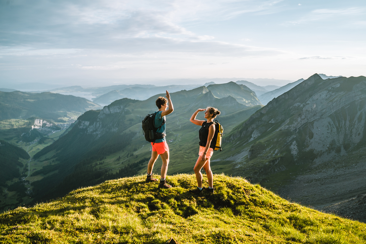 Zwei Personen stehen in einer gebirgigen Umgebung auf einem Berg und geben sich gerade ein "High Five".