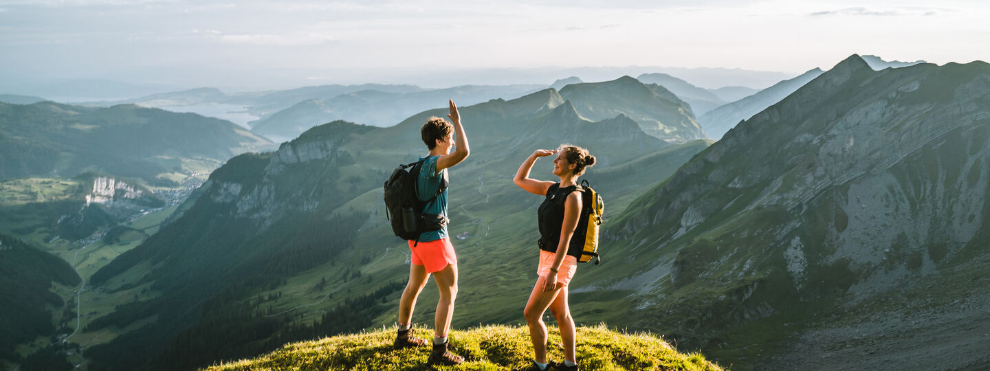 Zwei Personen stehen in einer gebirgigen Umgebung auf einem Berg und geben sich gerade ein "High Five".