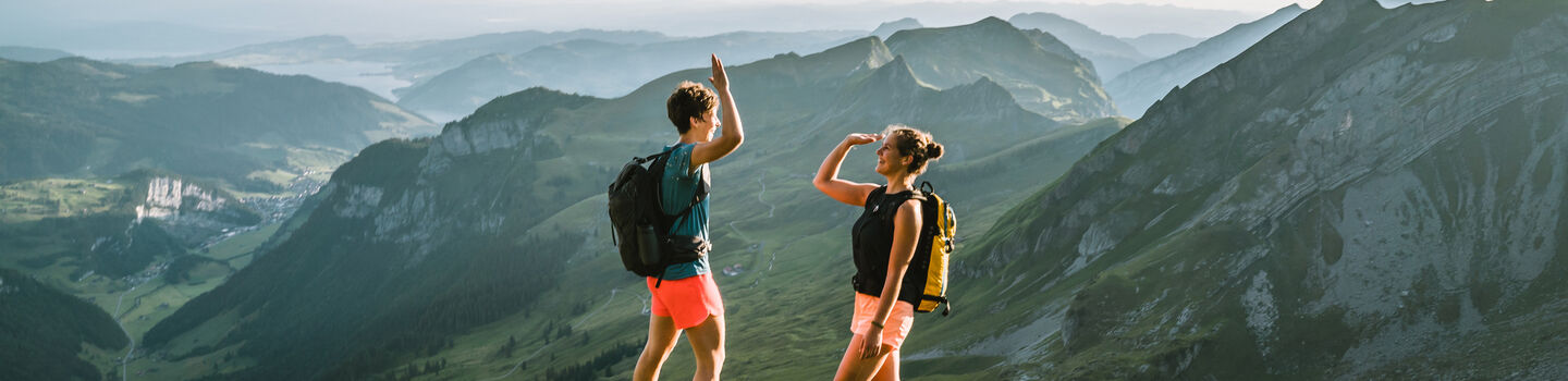 Zwei Personen stehen in einer gebirgigen Umgebung auf einem Berg und geben sich gerade ein "High Five".