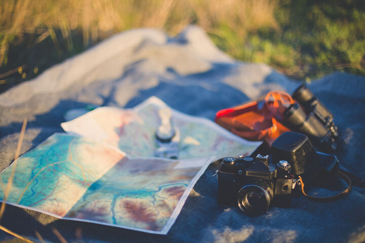 Auf einer Decke im Gras liegt eine Landkarte, eine Kamera, ein Fernglas und eine Taschenlampe.